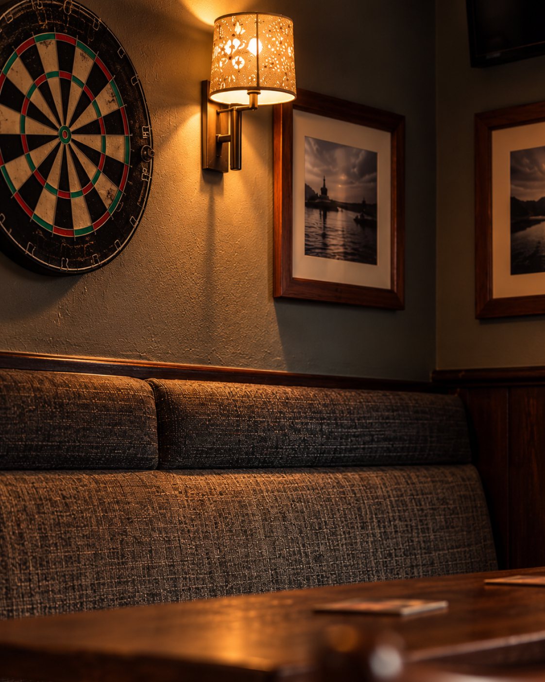 Dartboard beside framed pictures and booth seating at The Burgh Bar Dunoon