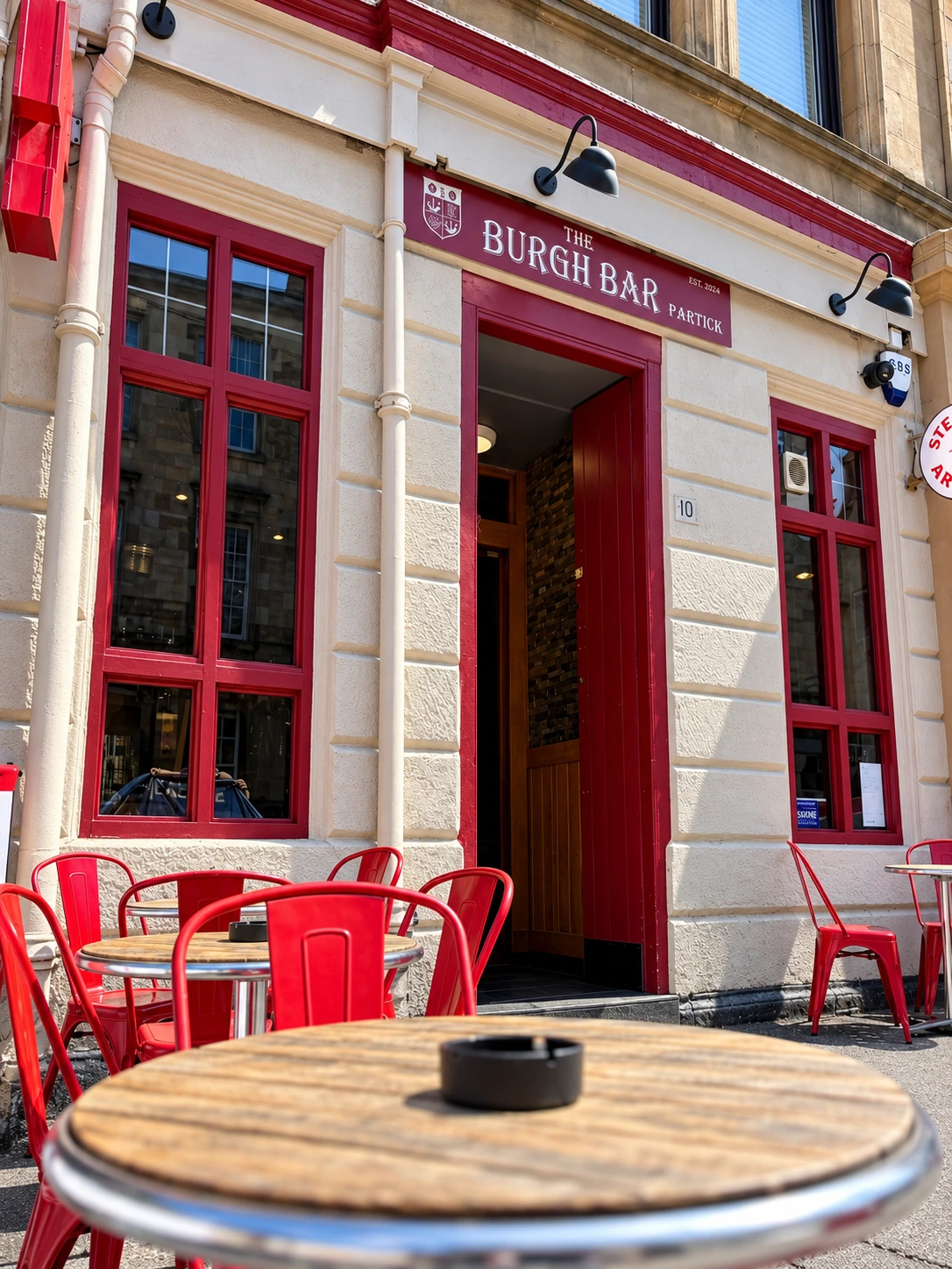 Red pub frontage and outside tables at The Burgh Bar in Partick, Glasgow