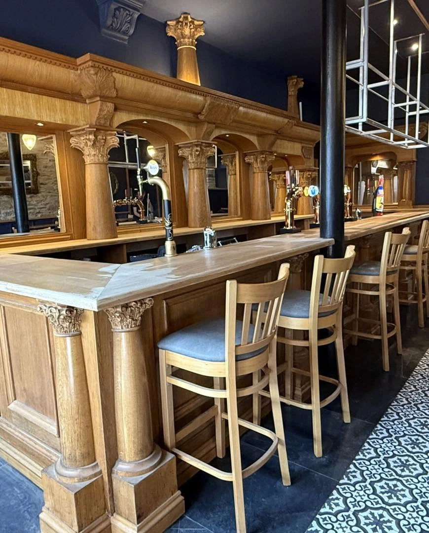 Ornate carved wooden bar and stools at Milne’s in Dunoon